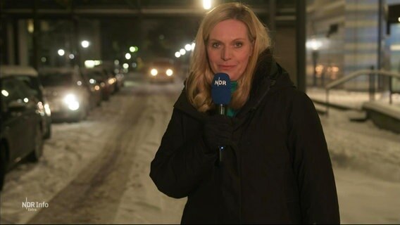 Juliane Möcklinghoff moderiert NDR Info extra "Schnee und Eis im Norden" am 05.12.2023. Die Moderatorin steht in einer Winterjacke im Freien. Hinter ihr erkennt man deutlich verschneite Straßen. © Screenshot 