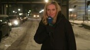 Juliane Möcklinghoff moderiert NDR Info extra "Schnee und Eis im Norden" am 05.12.2023. Die Moderatorin steht in einer Winterjacke im Freien. Hinter ihr erkennt man deutlich verschneite Straßen. © Screenshot 