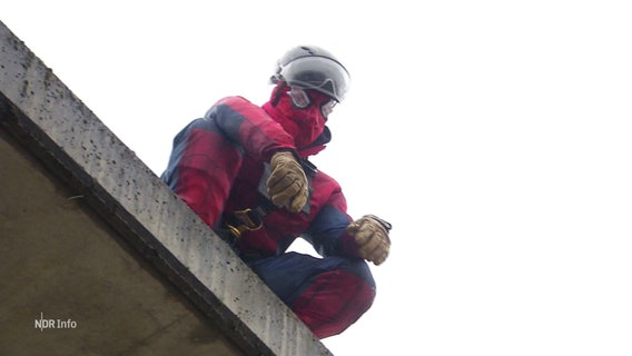 Ein Mensch im Spiderman-Kostüm hockt auf einem Flachdach. © Screenshot 