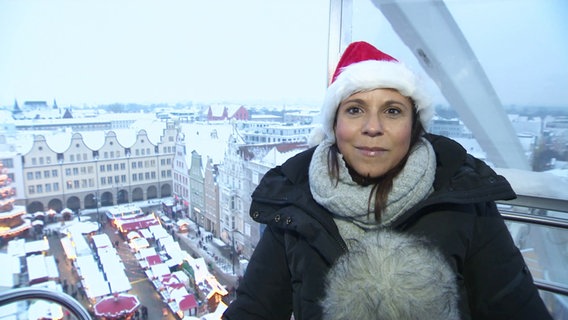 Tatjana Brand sitzt im Riesenrad mit dem Rostocker Weihnachtsmarkt im Hintergrund. © Screenshot 