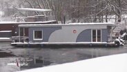 Ein eingeschneites Hausboot auf einem Kanal. © Screenshot 