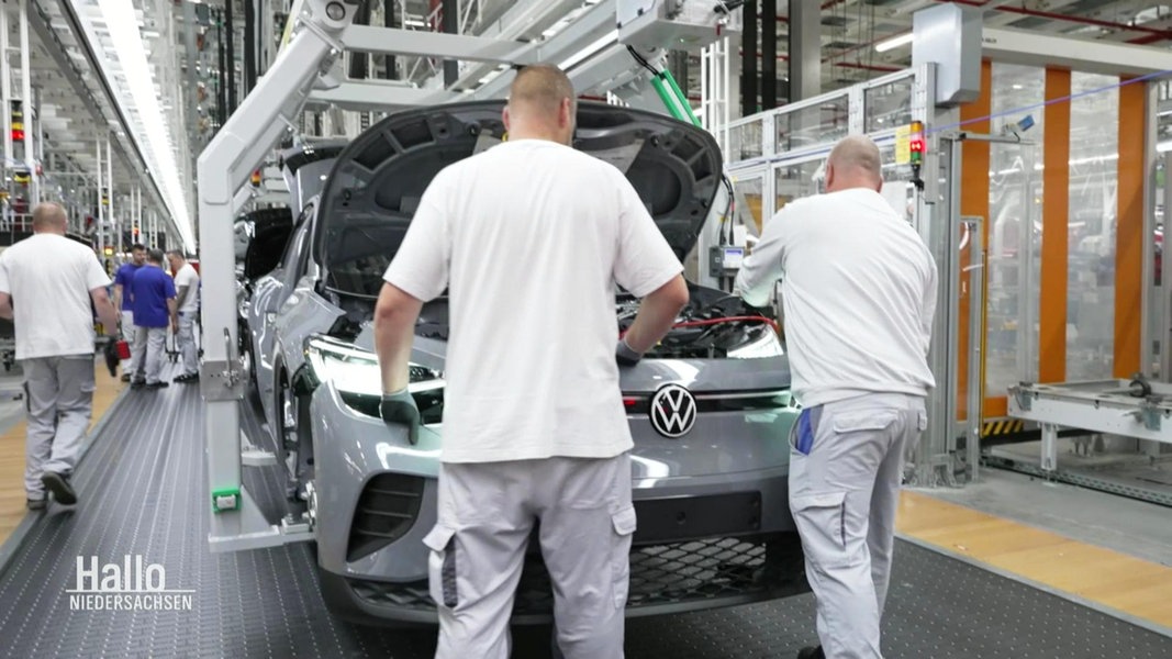 Zwei Angestellte stehen in einer VW Montagehalle und bauen ein Auto zusammen.