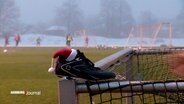 Ein Stollenschuh mit einer Nikolausmütze auf einem Torpfosten. Im Hintergrund das Training der Herren-Mannschaft des FC St. Pauli. © Screenshot 