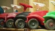 Fünf bunte, aneinandergereihte Bobbycars. © Screenshot 