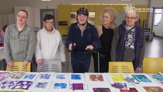 Fünf Menschen hinter einem Tisch, auf dem ihre Kunstwerke liegen. © Screenshot 