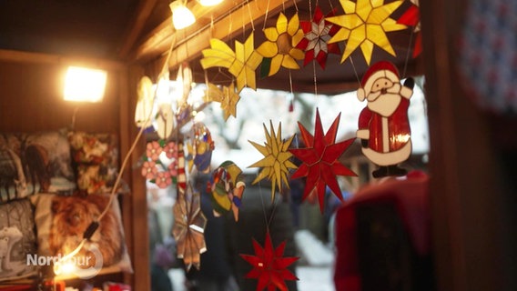 Blick aus einem Stand heraus, der hangemachte Dekorationsartikel verkauft. Von oben hängen gemalte Blumen und ein Comic-Weihnachtsmann zum Aufhängen. © Screenshot 