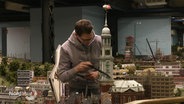 Ein Mann saugt das Modell des Hamburger Michels im Miniatur Wunderland ab. © Screenshot 