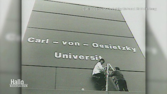 Archivaufnahme in schwarz, weiß: Studierende bekleben eine Hauswand mit dem Namen "Carl-von-Ossietzky Universität". © Screenshot 