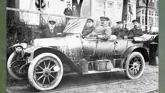 Eine Archivfotografie vom Beginn des 20. Jahrhunderts. In einem alten Auto sitzen vier Männer in Uniform und schauen stolz in die Kamera. © Screenshot 