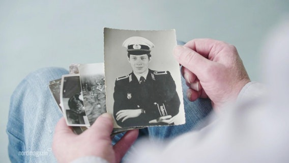 Eine Person hält Bilder eines Mannes in der Uniform der DDR-Volkspolizei in den Händen. © Screenshot 