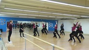 Tänzerinnen und Tänzer trainieren in einer Sporthalle. © Screenshot 