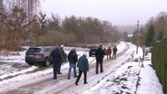 Eine Gruppe spaziert auf einer Dorfstraße. © Screenshot 