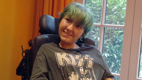 Der 18-jährige Cody (Geburstname Pia) im interview. Er sitzt in einem Rohlstuhl und lächelt. Der Pony seiner grün gefärbten Haare, hängt ihm ins Gesicht. © Screenshot 