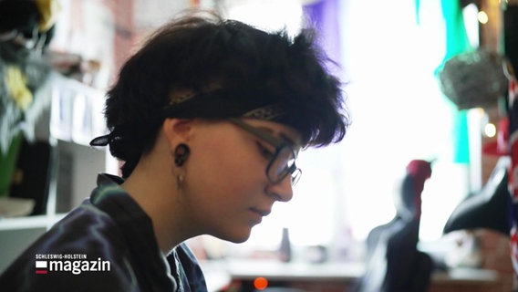 Ein Teenager mit dunklen Haaren und Brille ist von der Seite zu sehen. Er ein Tuch als Stirnband. © Screenshot 