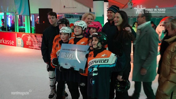 Gruppenfoto mit den Kindern der Neubrandenburg Blizzards und NDR-Moderation Thilo Tautz, Martina Scheller und Friderike Witthuhn in einer Eishalle. © Screenshot 