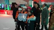 Gruppenfoto mit den Kindern der Neubrandenburg Blizzards und NDR-Moderation Thilo Tautz, Martina Scheller und Friderike Witthuhn in einer Eishalle. © Screenshot 