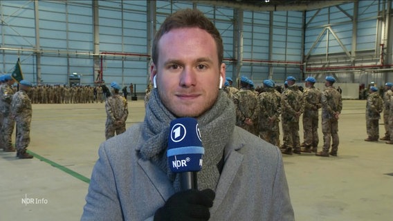 Reporter Tullio Puoti auf dem Fliegerhorst Wunstorf. Im Hintergrund Soldatinnen und Soldaten der Bundeswehr. © Screenshot 