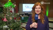 Eine NDR Reporterin berichtet live von der Spendenaktion, an der Seite steht ein geschmückter Tannenbaum. © Screenshot 