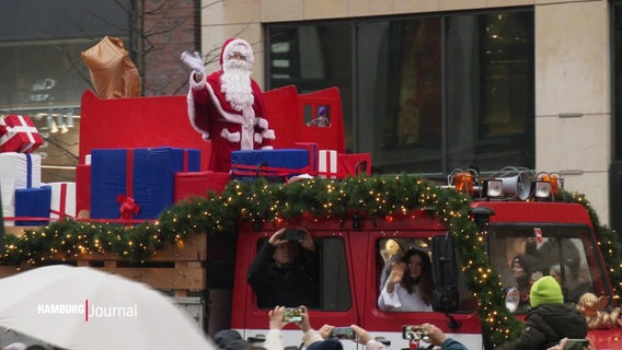 Ein Weihnachtsmann und ein Christkind winken Schaulustigen in der Hamburger Innenstadt von einem Weihnachtstruck zu. © Screenshot 