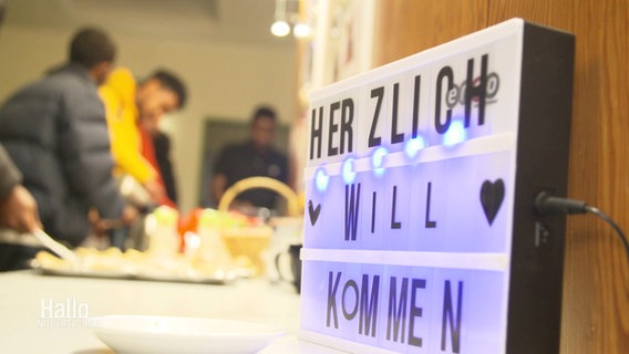 Auf einem lila leuchtenden Schild steht "Herzlich Willkommen". © Screenshot 