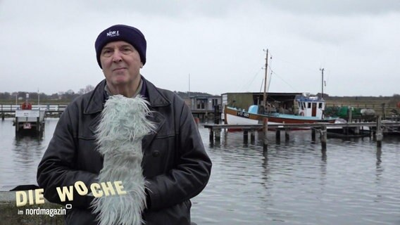 Wetterexperte Uwe Ulbrich spricht an einem kleineren Hafen in ein großes Mikrofon mit Windschutz. © Screenshot 