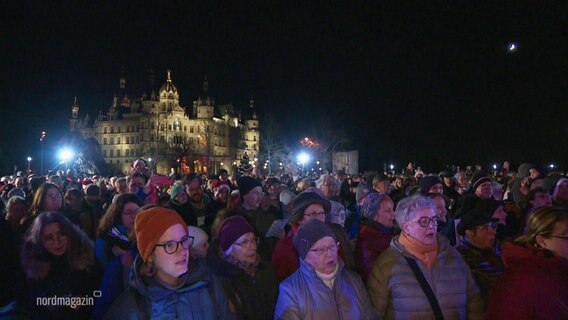 Vor dem Schweriner Schloss stehen viele hundert Menschen und singen gemeinsam bei Dunkelheit. © Screenshot 