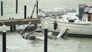 An einem Steg: Ein noch schwimmendes Segelboot, daneben schaut ein gesunkenes Boot kaum mehr aus dem Wasser. © Screenshot 