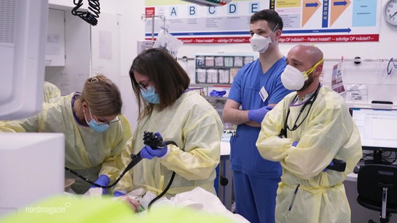 Fachpersonal mit Schutzmasken steht an einem Krankenbett in einer Klinik. © Screenshot 