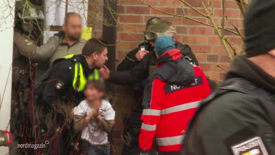 Menschen in einem Hauseingang, von denen viele von der Polizei sind. Ein Kind wird getragen. © Screenshot 