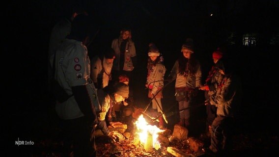 Eine Gruppe junger Pfadfinder steht an einem Lagerfeuer. © Screenshot 