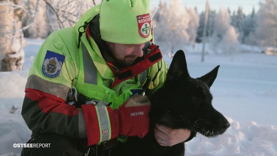 Ein Bergretter mit seinem Lawinensuchhund im Schnee. © Screenshot 