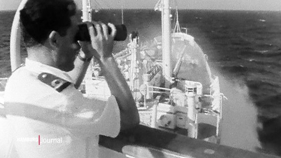 In einer alten Archivaufnahme blickt ein Mann auf einem Schiff durch ein Fernglas. © Screenshot 