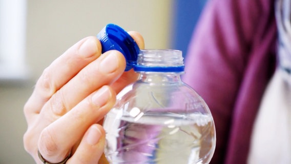 Eine Frau öffnet eine Wasserflasche aus Plastik. © Screenshot 