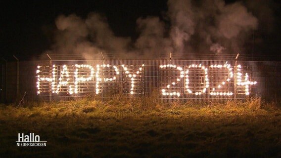 Ein leuchtender, aus Feuerwerkskörpern bestehender Schriftzug liest "Happy 2024". © Screenshot 