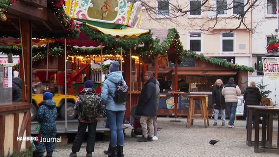 Blick auf einen kleineren Weihnachtsmarkt bei Tag: Neben ein paar Buden stehen einige Familien vor einem kleineren Karussell. © Screenshot 