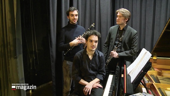 Die drei Musiker des Trios "ClariNoir" lehnen an einem Flügel bei einem Interview. © Screenshot 