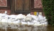 Vor einer Haustür liegen mehrere Schichten Sandsäcke um umliegendes Hochwasser abzuhalten. © Screenshot 