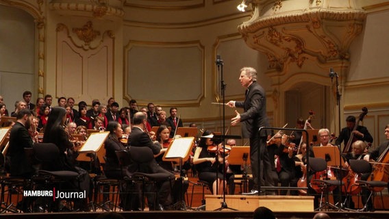Auf der Bühne der Hamburger Laeiszhalle steht ein Dirigent bei einem Konzert vor einem Orchester. © Screenshot 
