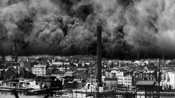 Originalaufnahmen in schwarz-weiß von Hamburg im Jahr 1945: Im Vordergrund sieht man Häuser, Kirchtürme und Schlote, im Hintergrund ist der Himmel verdunkelt von einer dunklen Wolke aus Asche und Explosionen. © Screenshot 