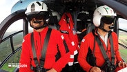 Pilot und Co-Pilot in roter Arbeitskleidung und Helmen in einem Hubschrauber. © Screenshot 