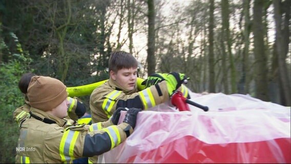 Junge Helferinnen der freiwilligen Feuerwehr befüllen einen mobilen Deich mit Wasser. © Screenshot 