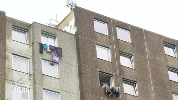 Ein grauer Hochhauskomplex. Vor manchen Fenstern hängen Wäscheständer mit Wäsche. © Screenshot 