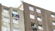 Ein grauer Hochhauskomplex. Vor manchen Fenstern hängen Wäscheständer mit Wäsche. © Screenshot 
