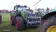 Ein großer Traktor ist für eine Demonstration vorbereitet: Am Trecker prangen ein Schild mit der Aufschrift "Wirtschaftselend Ampelregierung", eine auf Karton gemalte Ampel und ein Galgenstrick. © Screenshot 