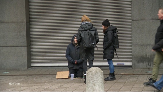 Die Sozialarbeiterin Sarah Menn und ihre Kollegin sprechen einen bettelnden Mann auf der Straße an, der am Boden kniet. © Screenshot 