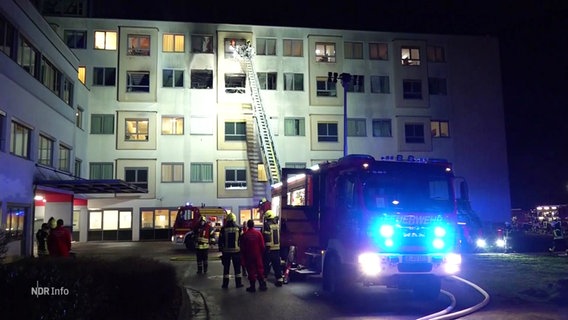 Ein Feuerwehrauto mit Blaulicht steht vor dem Helios Klinikum Uelzen. Eine Leiter führt zu den vom Brand betroffenen Stockwerken. © Screenshot 
