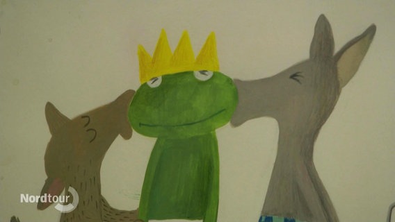 Zeichnung eines grünen Frosches mit einer Krone, der links und rechts von zwei grauen Tieren auf die Wange geküsst wird. © Screenshot 
