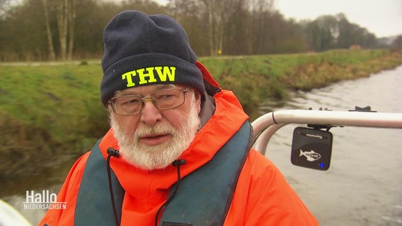 Jörg Bauer fährt auf einem Boot, er trägt eine Mütze mit der Aufschrift: "THW". © Screenshot 