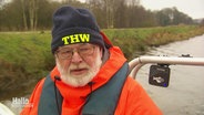 Jörg Bauer fährt auf einem Boot, er trägt eine Mütze mit der Aufschrift: "THW". © Screenshot 