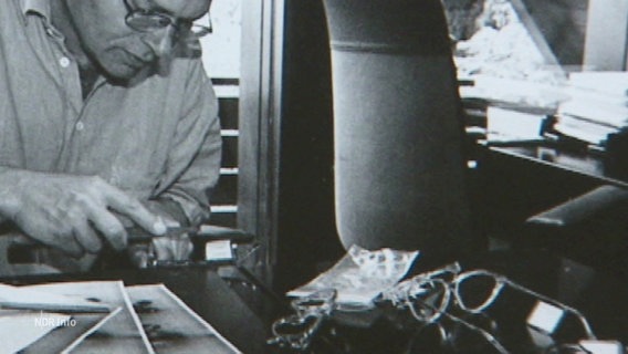 Schwarzweiß-Aufnahme von dem jungen Günther Fielmann, im Vordergrund liegen mehrere Brillen. © Screenshot 